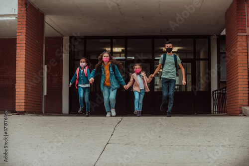 A group of students with protective masks on their faces run around the schoolyard while holding hands. Selective focus