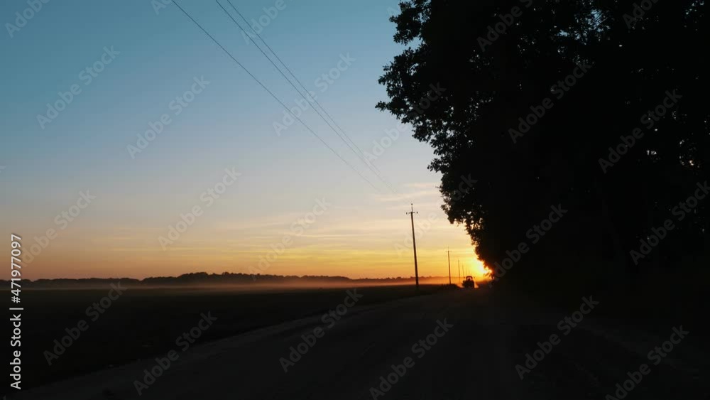 sunset over farm field. agricultural field at sunset. in the distance, the silhouette of a tractor is visible. the tractor is driving on a dirt road sunset over farm field. agricultural field at sunset. in the distance, the silhouette of a tractor is visible. the tractor is driving on a dirt road