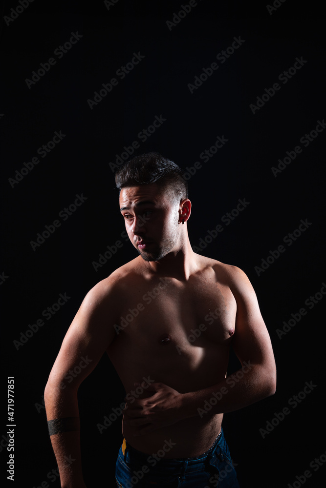 Young caucasian man shirtless in a photography studio with a backlight and a black background.