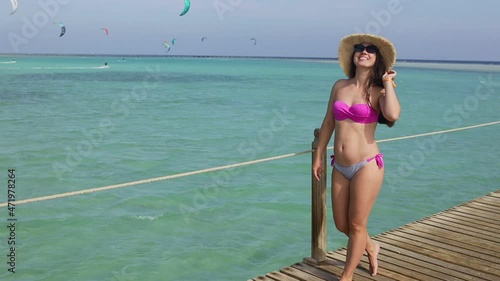 smiling young woman in sunglasses and straw hat walking on wooden pontoon