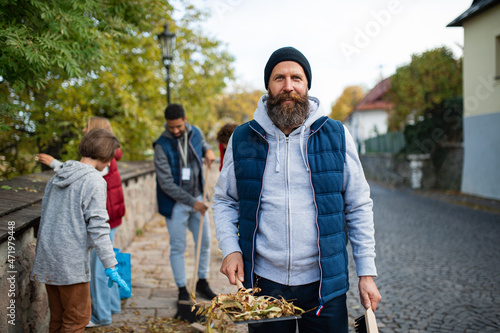 Mature man volunteer with team looking at camera and cleaning up street, community service concept