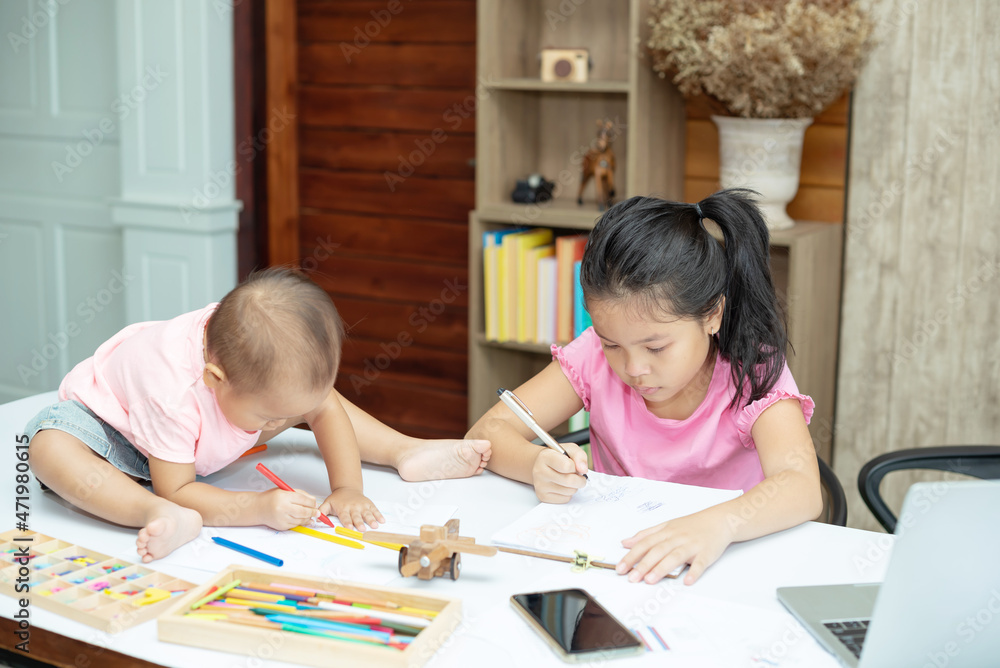 Little toddler girl sit on the working table, her older sister sitting and playing together while mother not home Little toddler girl sit on the working table, her older sister sitting and playing together while mother not home
