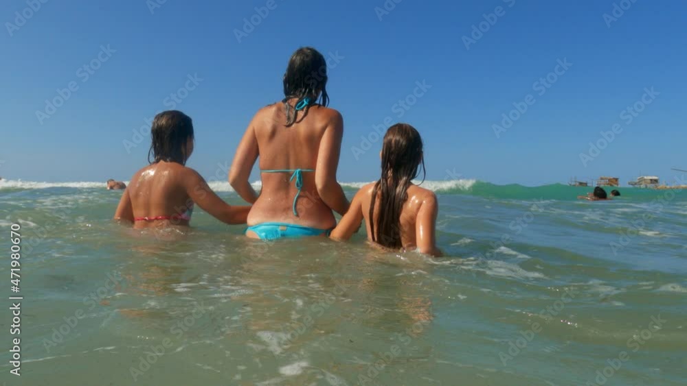 Rear view of woman with two child girls hand in hand have fun with big sea waves at Punta Penna in Abruzzo with trabocchi in background, Italy. Slow-motion Rear view of woman with two child girls hand in hand have fun with big sea waves at Punta Penna in Abruzzo with trabocchi in background, Italy. Slow-motion