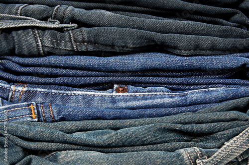 Stack of many blue jeans on the clothes shop shelf. Textile backgrounds and patterns