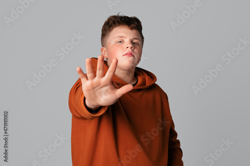 Confident serious teenager boy showing stop sign, lifting open palm and saying No