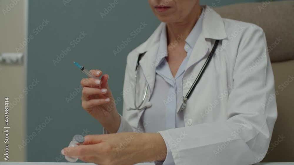 Midsection of female healthcare specialist taking medicine into syringe, preparing cure for making shot to patient indoors. Female doctor or nurse filling needle with vaccine in hospital Midsection of female healthcare specialist taking medicine into syringe, preparing cure for making shot to patient indoors. Female doctor or nurse filling needle with vaccine in hospital