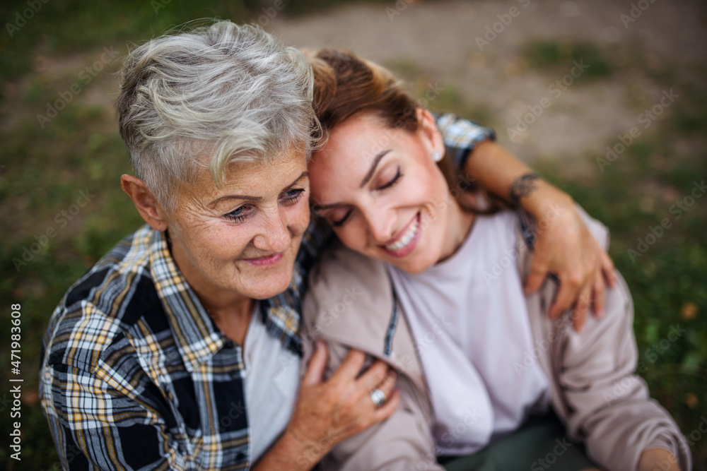 Close up of senior mother sitting on grass with adult daughter leaning her head on her outdoors. Close up of senior mother sitting on grass with adult daughter leaning her head on her outdoors.