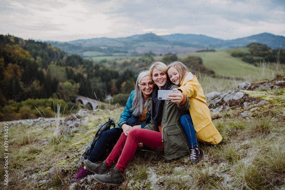 Small girl with mother and grandmother taking selfie outoors on top of mountain.