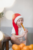 Boy playing wind musical instrument at home.child wearing Santa hat. On background gold Christmas lights. Online training, online classes.