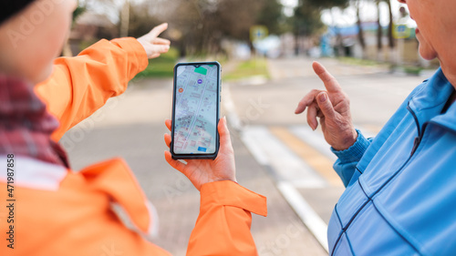 Slika na platnu A woman holds a smartphone with an online map and shows the way to an elderly woman with her hand