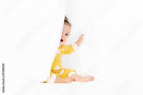 Cute baby in yellow pajamas peeking behind white sheet photo
