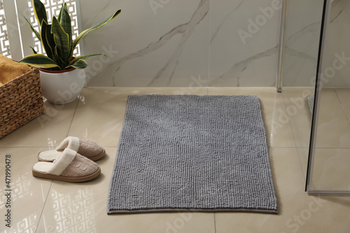 Soft grey bath mat and slippers on floor indoors