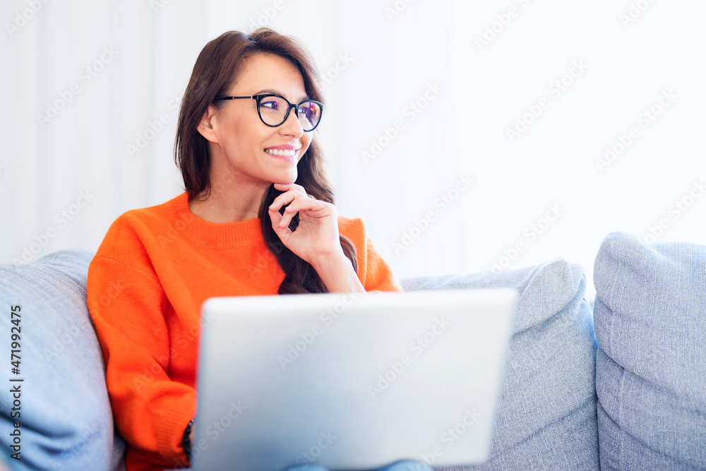 Happy woman using her laptop while sitting on the couch at home Happy woman using her laptop while sitting on the couch at home