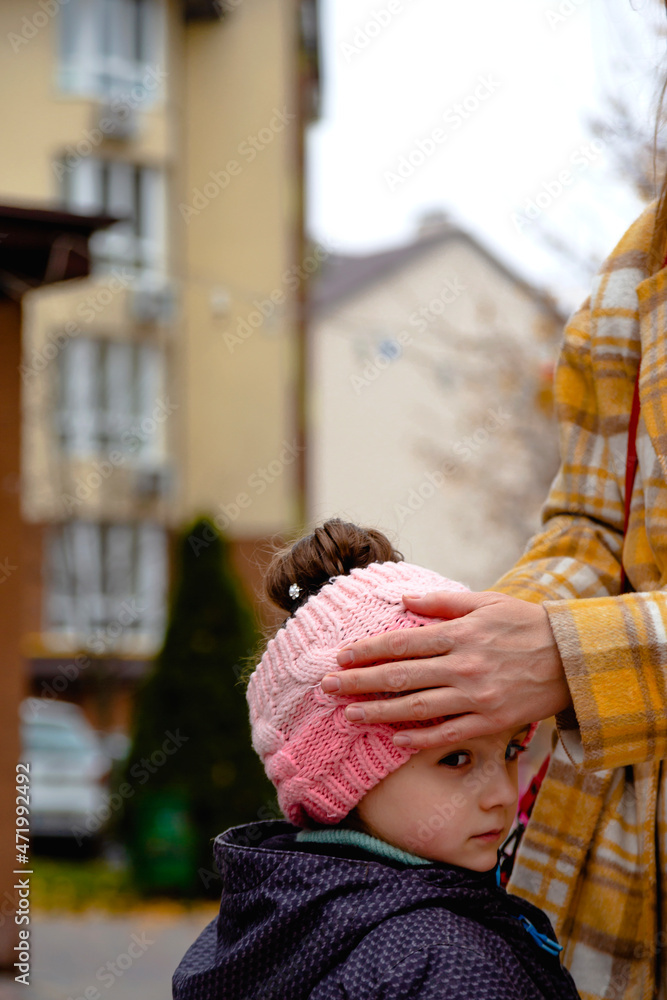 Mom straightens her daughter's hat and hair during an autumn walk. Fall colors
