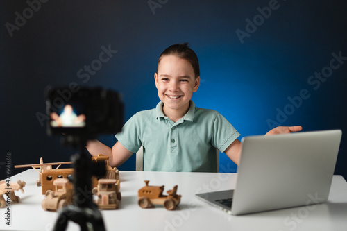 Kid blogger filming video on camera using the laptop, indoors. Online reviewing. Promoting eco wooden toys. Kid recording his gameplay for vlog.