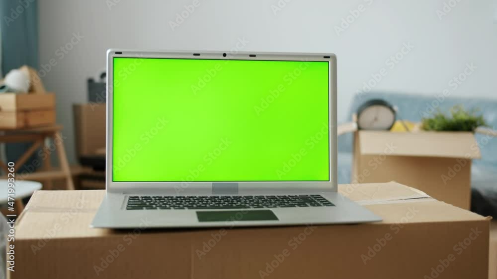 Close-up of green chroma key screen laptop on cardboard box in new house with no people in background. Modern technology and relocation concept. Close-up of green chroma key screen laptop on cardboard box in new house with no people in background. Modern technology and relocation concept.