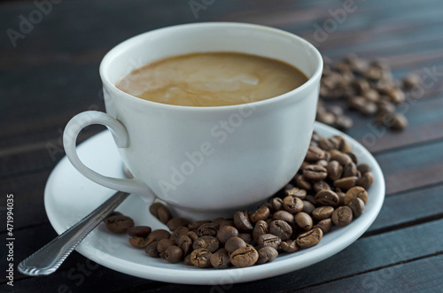 a cup of coffee with cream and coffee beans on a saucer.