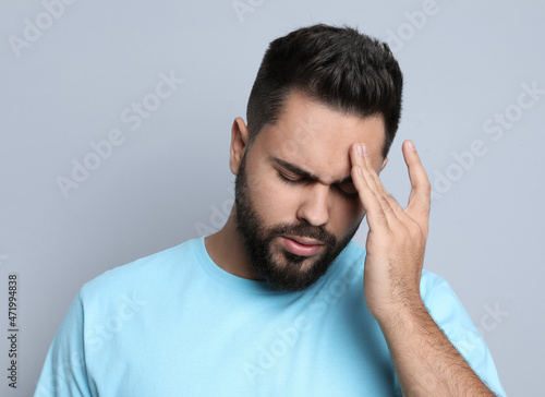 Young man suffering from headache on light grey background