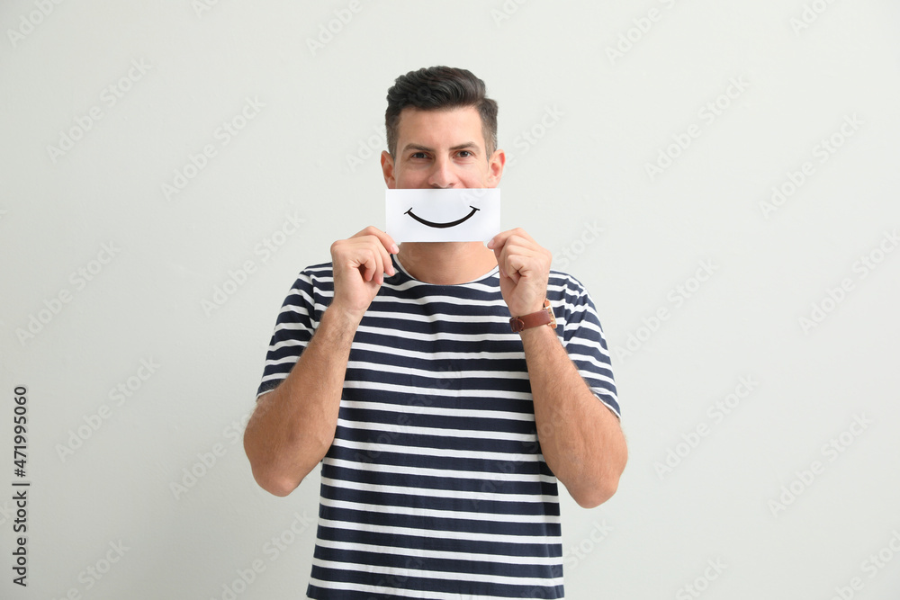 Man hiding emotions using card with drawn smile on white background Man hiding emotions using card with drawn smile on white background