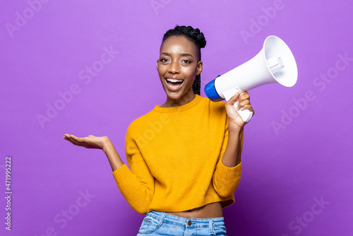 Portrait of smiling African American woman holding megaphone and opening hand in isolated purple studio background