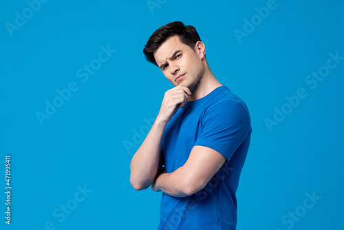 Young curious handsome Caucasian man thinking with hand touching chin in  isolated studio blue background photo