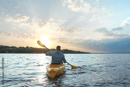 Man kayaking on river at sunset, back view. Summer activity
