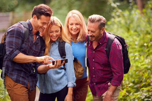 Group Of Friends Hiking In Countryside Looking At Picture On Phone As They Hike Along Path © Monkey Business