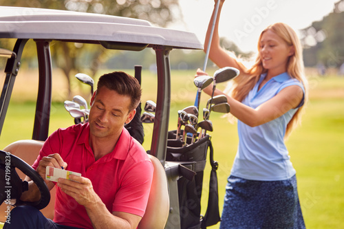 Couple Playing Round On Golf Together Sitting In Buggy With Score Card And Choosing Clubs © Monkey Business
