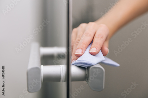 Cleaning glass door handles with an antiseptic wet wipe. Sanitize surfaces prevention in hospital and public spaces against corona virus. Woman hand using towel for cleaning home room door link.