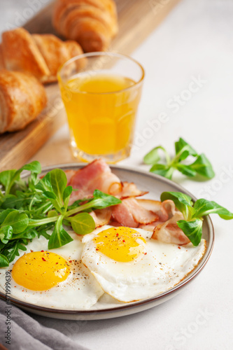 Continental breakfast - fried eggs, bacon and lettuce leaves in a plate on a bright background. Top View