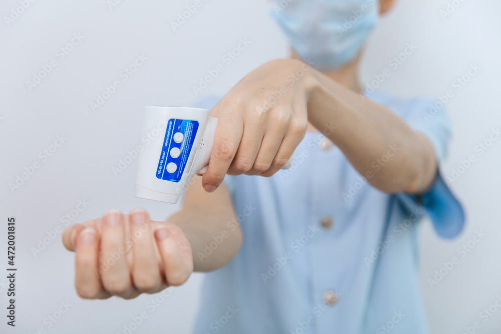 Temperature measurement gun in doctor hands. Close-up shot of doctor wearing protective surgical mask ready to use infrared isometric thermometer gun to check body temperature for virus symptoms.