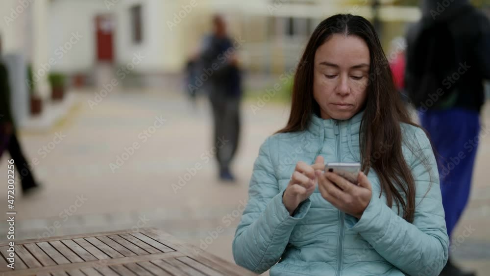 A beautiful adult is sitting at the table of an outdoor cafe, using a smartphone with the Internet to test online messages or social networks A beautiful adult is sitting at the table of an outdoor cafe, using a smartphone with the Internet to test online messages or social networks