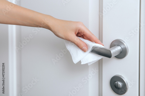 Cleaning door handles with an antiseptic wet wipe and gloves. Woman hand using towel for cleaning home room door link. Sanitize surfaces prevention in hospital and public spaces against corona virus.