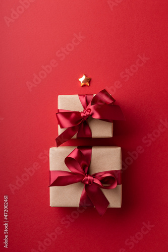 Two wrapped Christmas gift boxes tied red ribbons on red background.