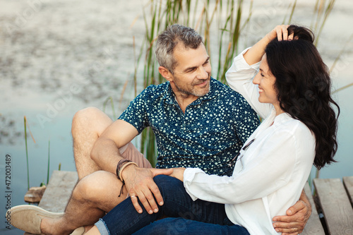 A mature married couple are sitting by the lake and hugging. happy lovers 50 years old