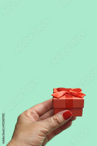 Mão de uma pessoa segurando um presente pequeno, embrulhado com papel e laço vermelhos com fundo verde claro. photo