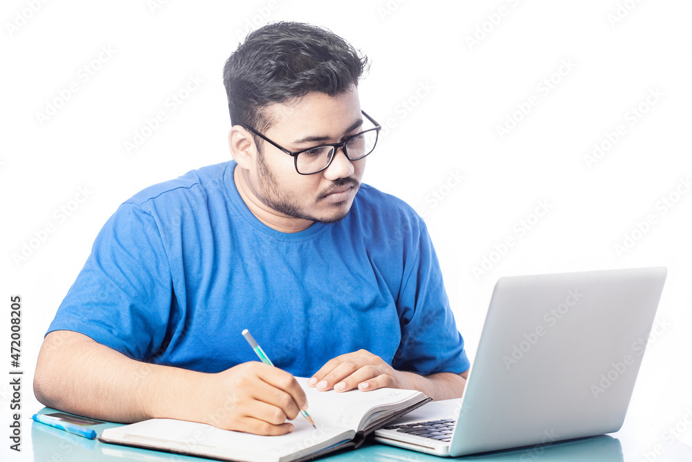 student writing on a notebook or diary while looking at laptop screen student writing on a notebook or diary while looking at laptop screen