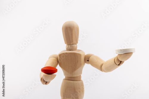 A wooden Gestalta doll or mannequin holds red and white pills in its hands on light background. The concept of choice. photo