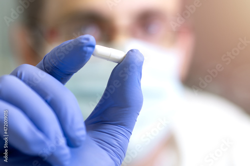 Scientist with medical mask showing white pill. Research concept. Selective focus.