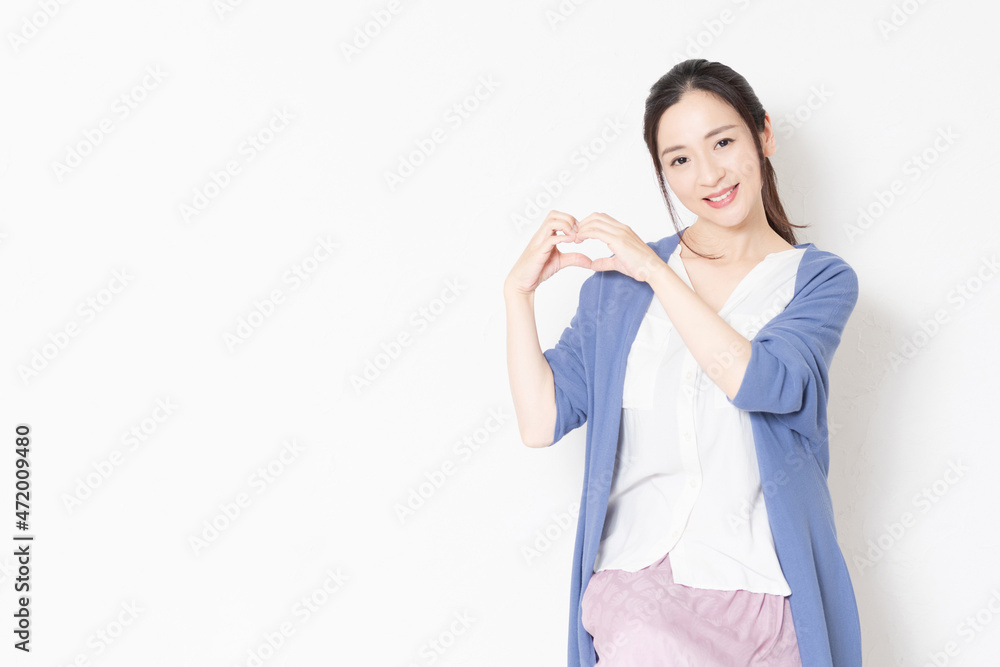 白い壁の前の椅子に座って手でハートの形を作る主婦 白い壁の前の椅子に座って手でハートの形を作る主婦
