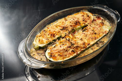 Baked zucchini filled with vegetables, feta cheese and parmesan in a glass casserole fresh from the oven, dark background with copy space, selected focus