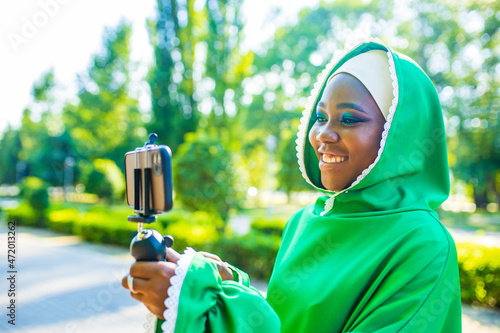 latin hispanic wonan in green muslim hijab with bright make up and nose piercing taking video stream outdoors summer park photo