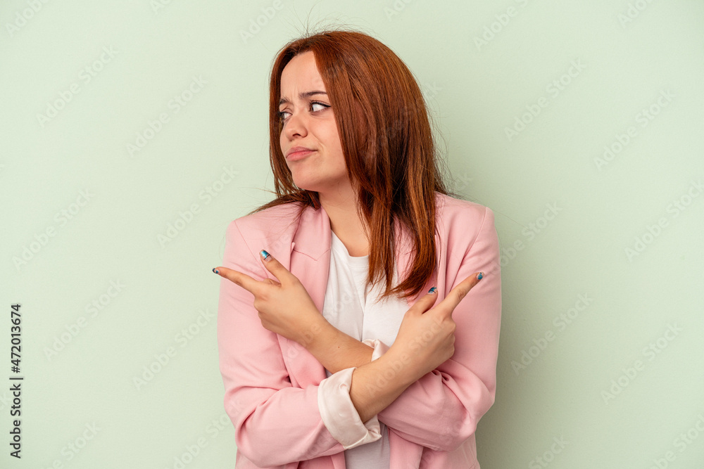 Young caucasian woman isolated on green background points sideways, is trying to choose between two options. Young caucasian woman isolated on green background points sideways, is trying to choose between two options.