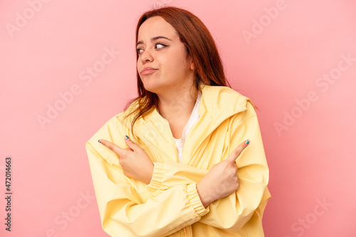 Young caucasian woman isolated on pink background points sideways, is trying to choose between two options. © Asier