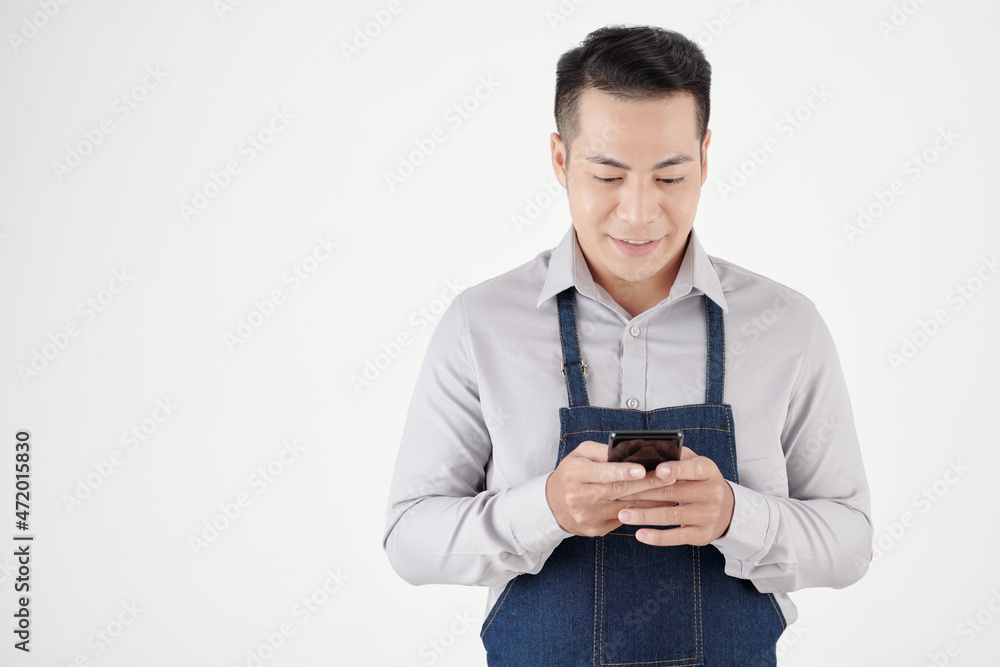 Smiling young barista checking notifications and answering text messages on smartphone Smiling young barista checking notifications and answering text messages on smartphone