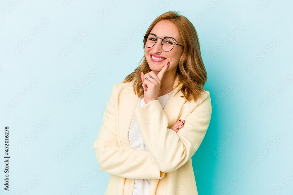 Young caucasian woman isolated on blue background smiling happy and confident, touching chin with hand. Young caucasian woman isolated on blue background smiling happy and confident, touching chin with hand.