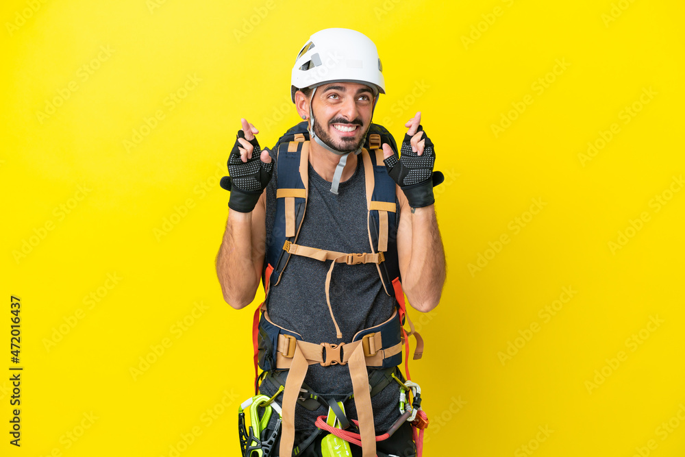 Young caucasian rock climber man isolated on yellow background with fingers crossing Young caucasian rock climber man isolated on yellow background with fingers crossing