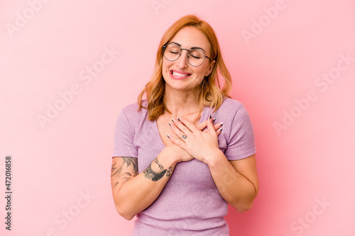 Young caucasian woman isolated on pink background has friendly expression, pressing palm to chest. Love concept.