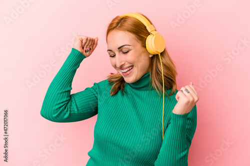 Young caucasian woman listening to music isolated on pink background