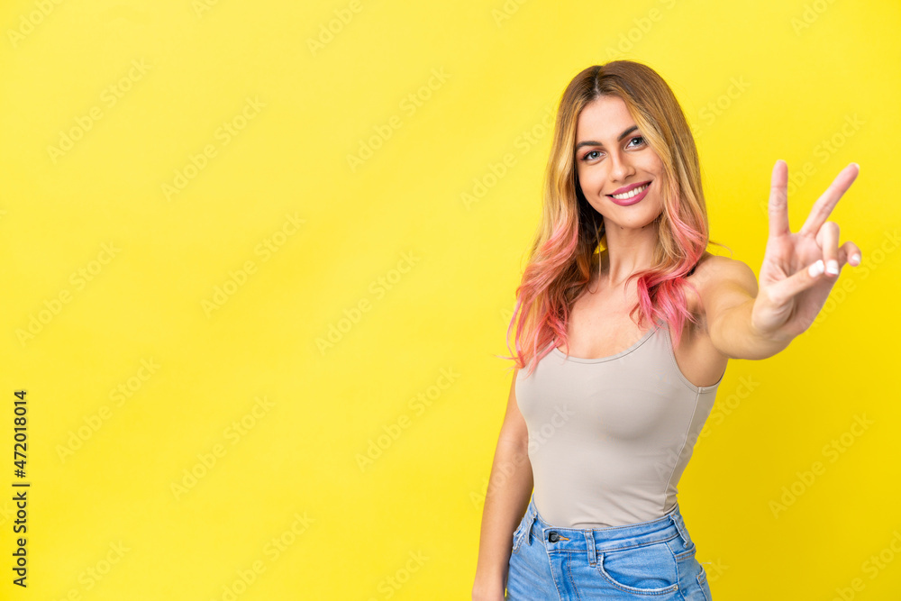 Young woman over isolated yellow background smiling and showing victory sign Young woman over isolated yellow background smiling and showing victory sign